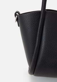 Czarna skórzana torba na ramię o fakturowanej powierzchni, zwężającym się kształcie i pojedynczym pasku na ramię, z akcentem w postaci srebrnego metalowego pierścienia.