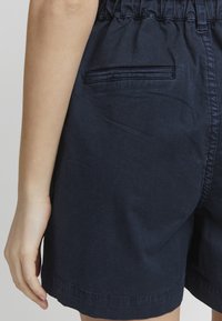Pantalones cortos de algodón navy con cinturilla elástica, que cuentan con un bolsillo trasero y un dobladillo recto. Textura suave, diseño casual, hasta la rodilla.