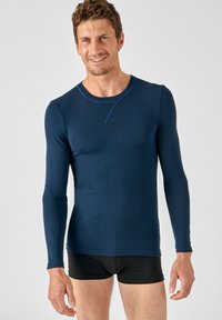 Maglietta a maniche lunghe base layer di colore blu navy realizzata in tessuto elasticizzato, con colletto rotondo e cuciture a contrasto, e un design aderente.