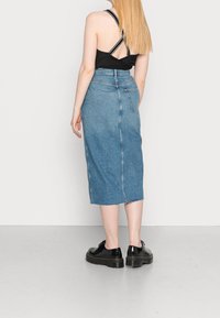 Falda midi de denim con dobladillo sin acabar, lavado azul medio, detalle en la costura trasera y una silueta ajustada, combinada con zapatos de plataforma negros.