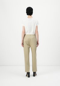 Λευκό κοντομάνικο T-shirt συνδυασμένο με μπεζ κομμένα παντελόνια και μαύρες block-heeled γόβες, με θέα από πίσω σε λευκό φόντο.