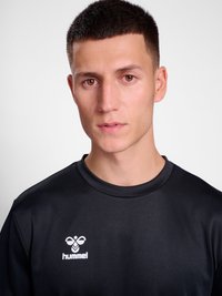 Ung mand med kort mørkt hår iført en sort Hummel sportstrøje, vendt frem mod en ensfarvet lys baggrund.