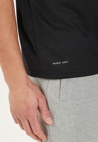 Schwarzes, schnell trocknendes Shirt aus strukturiertem Stoff, mit weißem, bedrucktem Text "QUICK DRY" am unteren Saum, kombiniert mit grauen Sweatpants.