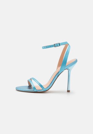 Blaue High-Heels-Sandale mit glänzendem Finish, schlankem Absatz, Knöchelriemen und zwei dekorativen, genagelten Riemen über der Vorderseite.