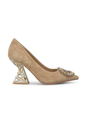 Chaussure à talon haut en daim beige avec bout pointu, ornée de grosses pierres sur le bout et d’un talon à la forme unique décoré de cristaux.
