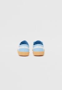Blue canvas shoes with white stripes, featuring a textured gum rubber sole. Rounded shape with a low profile, designed for comfort and stability.