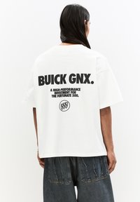 Hvid bomulds t-shirt med et iøjnefaldende sort grafisk tekst på bagsiden, der siger "BUICK GNX" og et cirkulært logo nedenfor. Løs pasform.