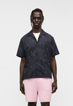 Camicia blu navy a maniche corte con righe bianche e ricami, abbinata a pantaloncini rosa chiaro con texture. Vestibilità standard e design con bottoni.