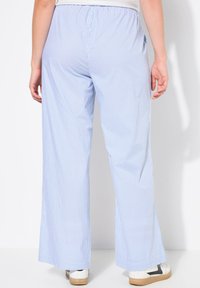 Pantalons larges rayés bleus et blancs avec une taille élastique, offrant une coupe décontractée et des poches latérales. Portés avec des baskets blanches.