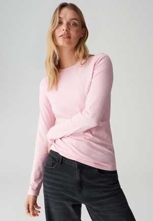 Roze T-shirt met lange mouwen gemaakt van zacht materiaal, met een ronde halslijn en een aansluitend model, gecombineerd met een donkere jeans.