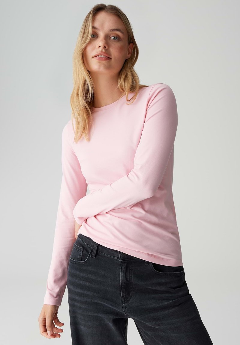 Langärmliges rosa T-Shirt aus weichem Stoff, mit Rundhalsausschnitt und figurbetontem Schnitt, kombiniert mit dunklen Jeans.