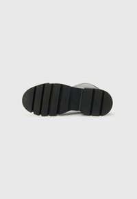 Suela de goma negra con textura estriada y relieves pronunciados, diseñada para tracción y durabilidad. Perfil plano con ligera curva en la puntera.