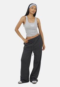 Szara koszulka na ramiączkach z napisem "NEW YORK", w połączeniu z luźnymi ciemnoszarymi spodniami dresowymi. Model ma na sobie pasującą szaro-czarną opaskę na głowę i jasne obuwie.