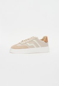 Basket beige en matériaux en daim et cuir, semelle blanche et rayures crème. Comprend un contrefort beige et des lacets beiges.