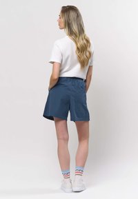 Laivastonsiniset rentoistaiset shortsit sivutaskuilla, yhdistettynä valkoiseen ribbineulottuun t-paitaan ja valkoisiin tennareihin, joissa on moniväriset sukat.