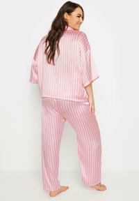 El conjunto de pijama de satén a rayas rosas y blancas presenta una camiseta de corte holgado con mangas cortas y pantalones de pierna ancha con una textura suave y lisa.