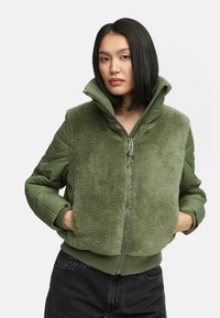 Green bomber jacket featuring a plush, textured fleece front and smooth fabric sleeves. Zipper closure and ribbed hem. High collar.
