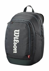 Sac à dos en tissu gris avec plusieurs compartiments zippés, arborant un grand logo blanc "Wilson", une surface texturée et des bretelles rembourrées.