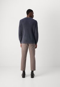 Marineblå, ribbestrikket genser med lange ermer, sammen med lyse beige bukser og svarte ankelstøvler. Bakview av antrekket.