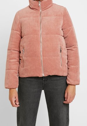 Lyserød kordfløjls-pufferjakke med frontlynlås og lynlåslommer i siderne, båret med mørkegrå jeans.