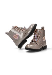 Botas de tobillo plateadas brillantes con un acabado brillante, parches de corazones rosa y dorado, y un adorno decorativo similar a joyas en los cordones. Suela de goma negra.