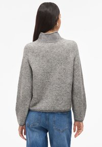 Suéter cinza em padrão espinha de peixe, com gola alta, mangas longas e um corte descontraído, combinado com jeans azul.