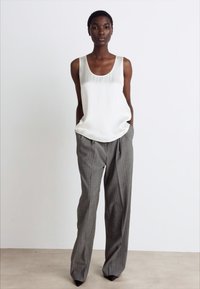 Valkoinen satiinitoppu, jossa on pyöreä pääntie, yhdistettynä harmaisiin raidallisiin korkeavyötäröisiin housuihin, joissa on löysä istuvuus ja hienovaraiset laskokset.