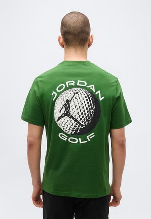 Άτομο με κοντά μαλλιά γυρισμένο πλάτη, φοράει πράσινο μπλουζάκι με μεγάλη ασπρόμαυρη εικόνα από μπάλα γκολφ και κείμενο "Jordan Golf".