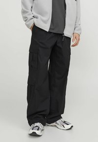 Pantaloni cargo neri realizzati in tessuto resistente, con molteplici tasche, vestibilità rilassata e vita con cordoncino. Abbinati a sneakers bianche e nere.