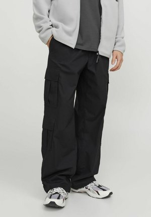 Pantalons cargo noirs en tissu durable, avec plusieurs poches, coupe décontractée et taille à cordon. Associés à des baskets blanches et noires.