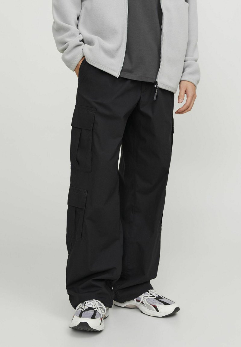 Pantaloni cargo neri realizzati in tessuto resistente, con molteplici tasche, vestibilità rilassata e vita con cordoncino. Abbinati a sneakers bianche e nere.