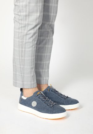 Blaue Canvas-Sneaker mit weißen Gummisohlen, grauen Schnürsenkeln und gelben Akzenten. Kombiniert mit grau karierten Hosen mit einer maßgeschneiderten Passform.