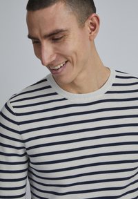 Pull en coton crème avec des rayures horizontales bleu marine. Doté d'un col rond et de poignets côtelés. Texture lisse avec un design classique.