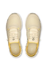 Beige sporta apavi ar acs audumu, teksturētu dizainu un dzelteniem akcentiem. Iezīmes noapaļota purngala un viegla, mīksta zole.
