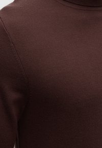 Gros plan d'un pull en maille marron foncé montrant la texture du tissu et la couture de l'épaule avec un col rond.