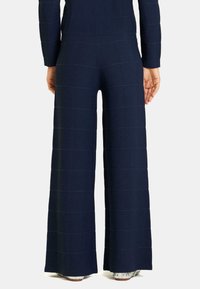 Pantalons larges marine en tissu texturé, avec des nervures horizontales et une taille haute. L'ourlet est fini avec une bordure nette.