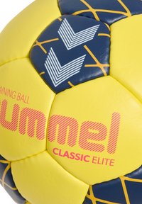Gul träningsboll med blå accenter, med ett geometriskt mönster, texturerad yta och röd logotyp "Hummel CLASSIC ELITE."