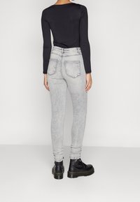 Grå skinny jeans med en urtvättad finish, med bakfickor och medelhög midja. Bärs med en långärmad svart topp och svarta stövlar.