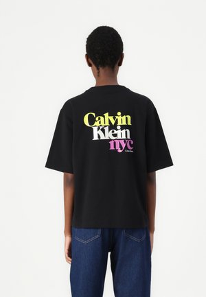 Black cotton t-shirt featuring multicolored "Calvin Klein" and "nyc" text on the back, short sleeves, and a relaxed fit.
