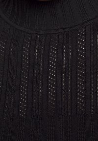 Pull en maille noire avec une texture côtelée et des rayures verticales étroites alternées avec de petites découpes. Design à col montant.