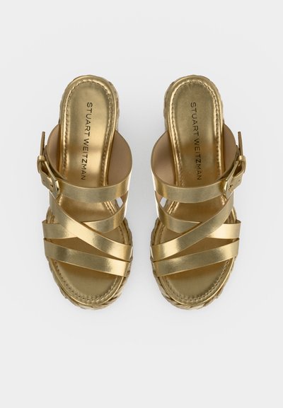 Sandales compensées dorées métalliques à brides avec fermeture à boucle et détail tressé sur la semelle, marquées "Stuart Weitzman" sur la semelle intérieure.