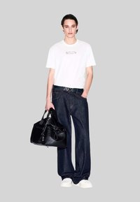 Weißes T-Shirt mit aufgedrucktem Text, dunkelblaue weit geschnittene Jeans, schwarze strukturierte Handtasche und weiße Sneakers. Schlichte Farbpalette und modernes Design.