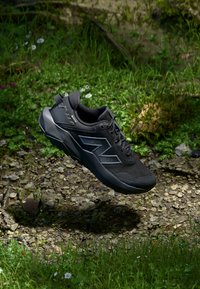 Schwarzer Sportschuh mit einem strukturierten Mesh-Obermaterial, auffälligem Seitenlogo und einer robusten Sohle. Das Design weist kantige Akzente und eine gepolsterte Kragenpartie auf.