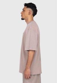 T-shirt oversize beige clair à côtes avec des manches courtes, présentant un col rond et un motif texturé subtil, mis en avant sur un modèle de profil.