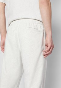 Pantaloni della tuta grigio chiaro realizzati in morbido tessuto, con vita elasticizzata, una tasca posteriore e vestibilità comoda. Ideali per un look informale.