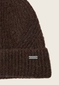 Bonnet en tricot marron en laine texturée, avec un bord côtelé et une étiquette argentée "TOM TAILOR" sur le revers.