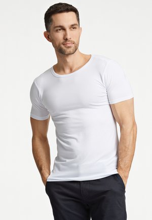 Witte t-shirt met korte mouwen van gladde stof, met een ronde hals en een aansluitend ontwerp, gedragen met een donkere broek.