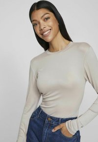 Beige långärmad topp med rund halsringning, smal passform och slät yta, kombinerad med blå högmidjade jeans i denim med en knapp.