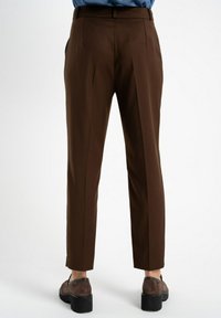 Brązowe spodnie o dopasowanym kroju z prostymi nogawkami, z tylnymi kieszeniami i gładką teksturą. Slim fit, zwężane w okolicy kostek.