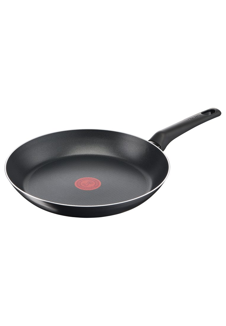 Sartén negra con un revestimiento antiadherente, forma redonda y un emblema rojo en el centro. Presenta un mango de plástico negro.
